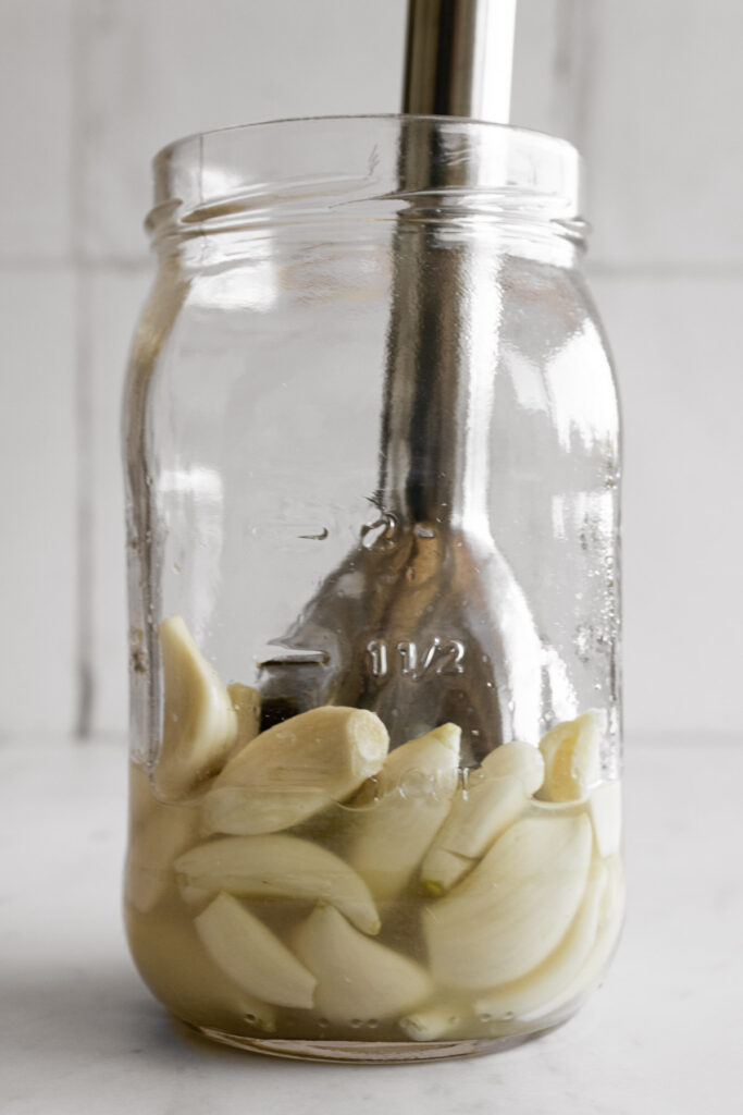 Garlic, lemon juice, and salt in a mason jar with an immersion blender in the jar