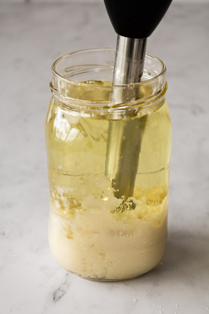 Jar with garlic paste topped with oil and immersion blender in the jar