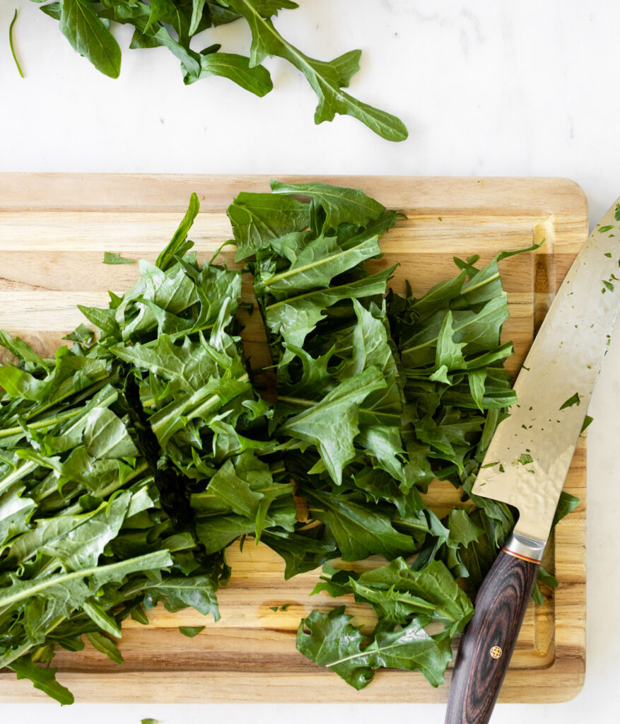 chopped dandelion greens on a wooden cutting board with a chef's knife on the side