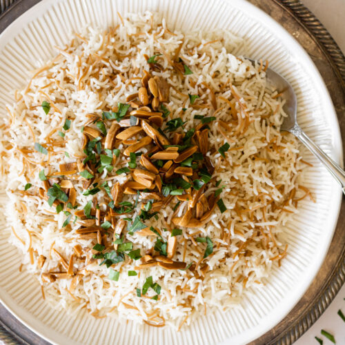 rice with toasted vermicelli garnished with toasted almonds and chopped parsley on a white plate with a spoon