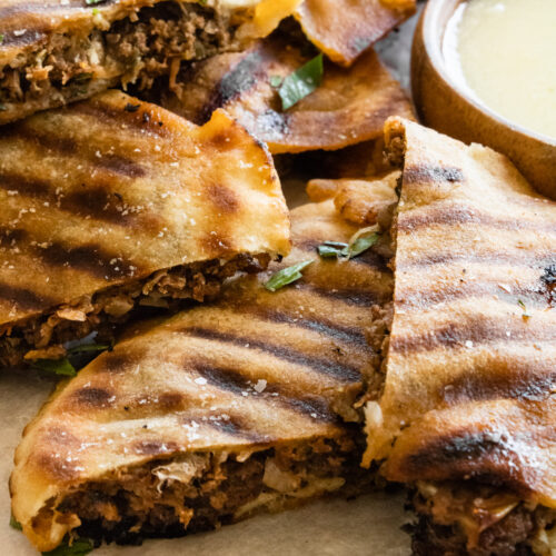 grilled arayes with cheese on a cutting board with garlic sauce on the side.