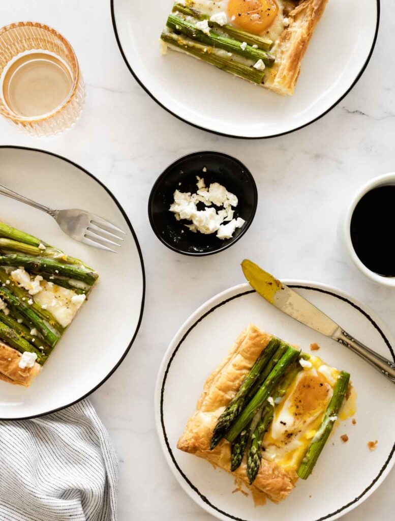 three plates with asparagus puff pastry tart with eggs and feta with a cup of coffee and a glass of water.