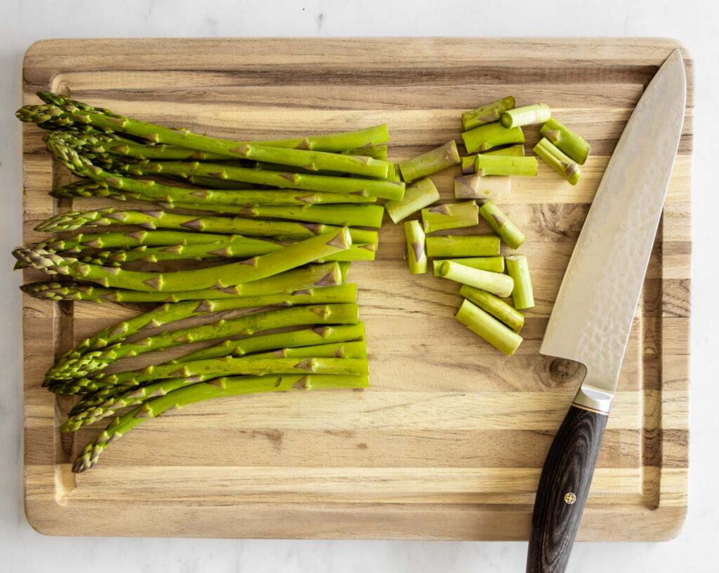 asparagus ends trimmed on a wooden cutting board with a knife on the side.