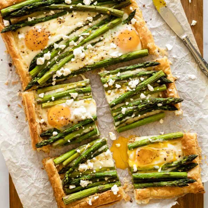 asparagus puff pastry tart with a runny egg yolk oozing and feta cheese crumbles on a wooden board.