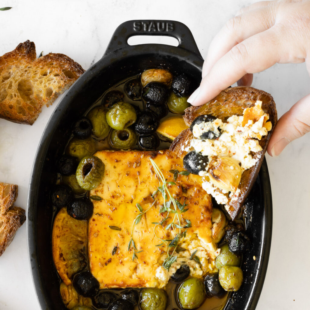 hand picking up bread with baked feta with olives and honey.