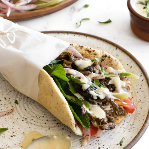 beef and lamb shawarma wrap on a plate with a spoon in tahini sauce and the vegetables on the side.