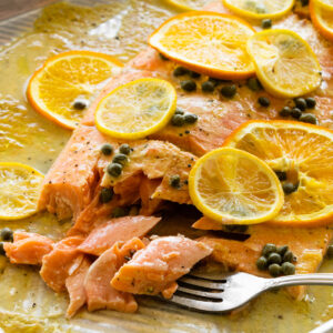 close up of slow roasted salmon with citrus and capers on a baking sheet with a fork.