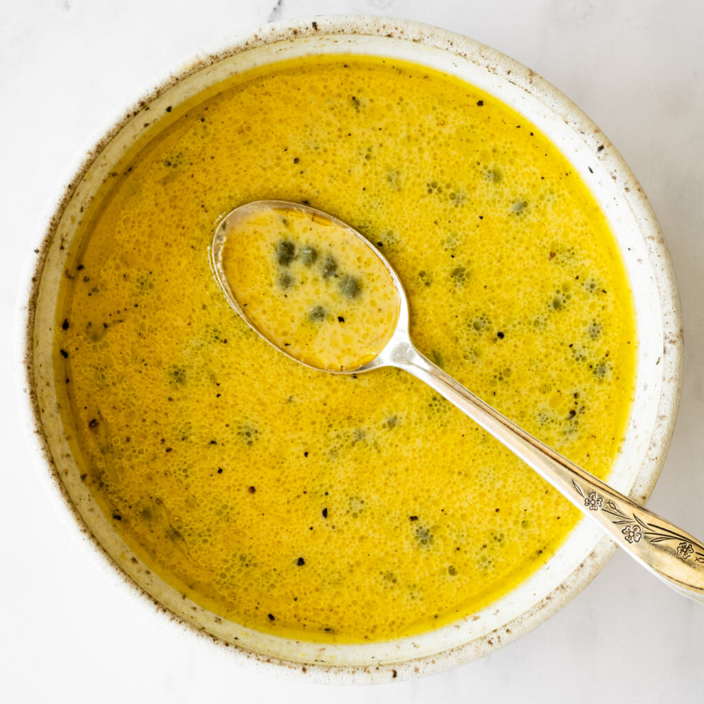 citrus and caper sauce in a ceramic bowl with a spoon in the middle.