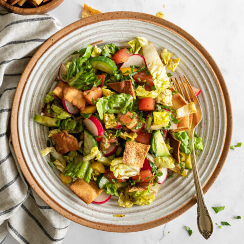 authentic fattoush salad in a ceramic bowl with a fork and linen and extra pita chips on the side.