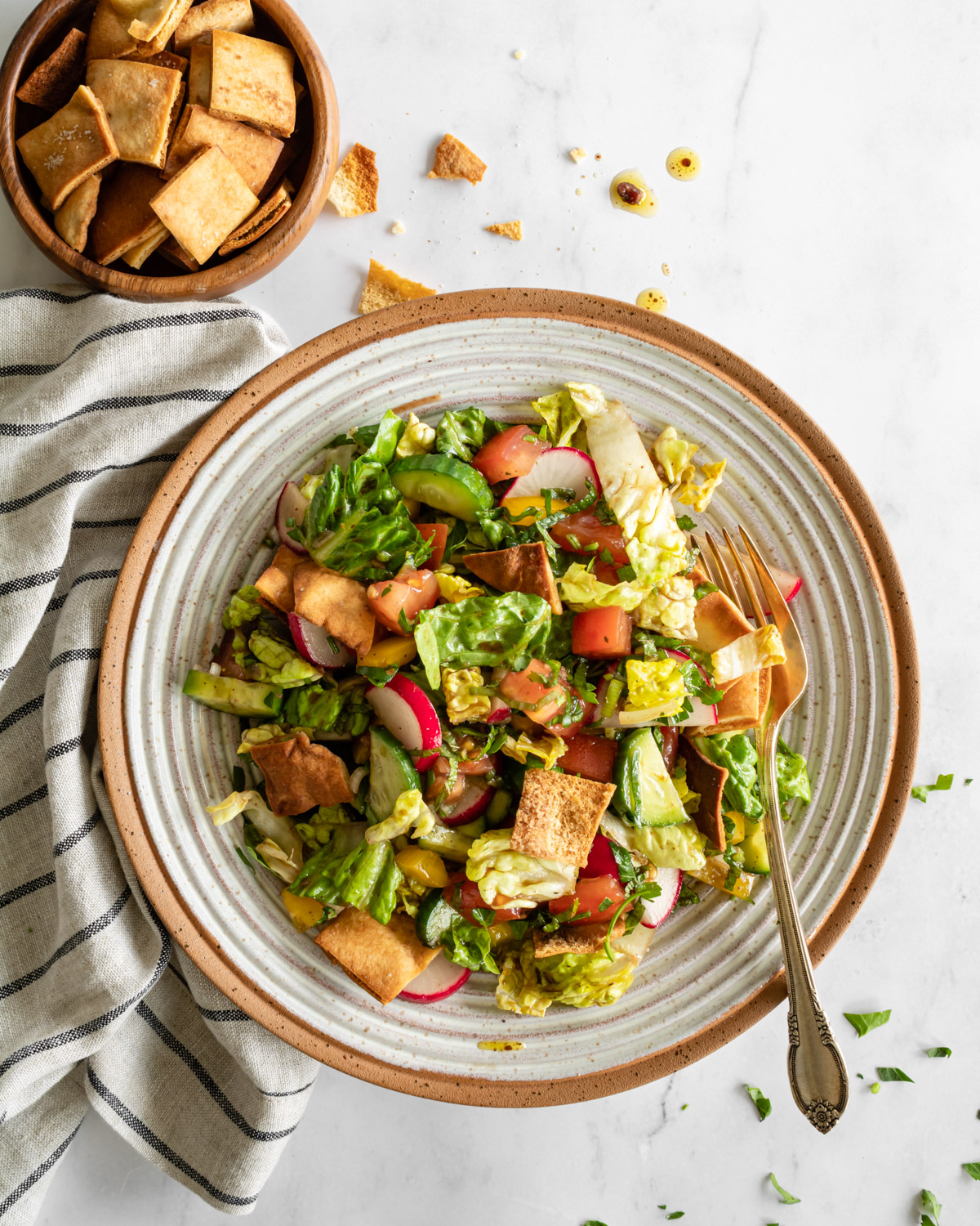 authentic fattoush salad in a ceramic bowl with a fork and linen and extra pita chips on the side.