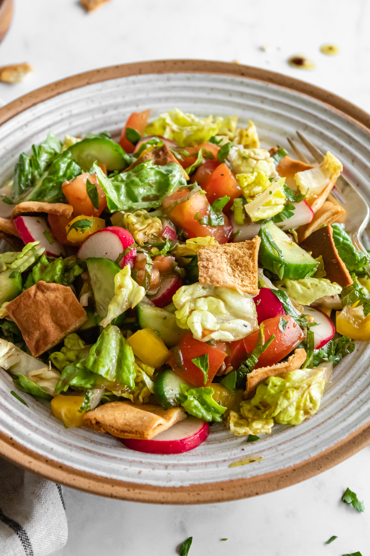 close up of fattoush salad in a ceramic bowl with a linen on the side.