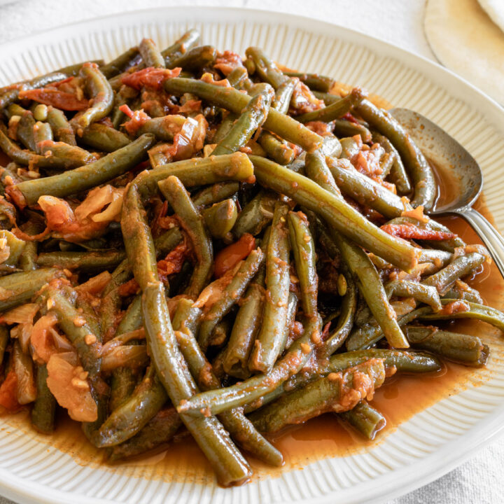 close up of lebanese green beans in a white plate with a spoon.
