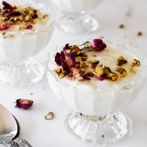 close up of lebanese rice pudding in decorative glass dishes with crushed pistachios and dried rose petals.