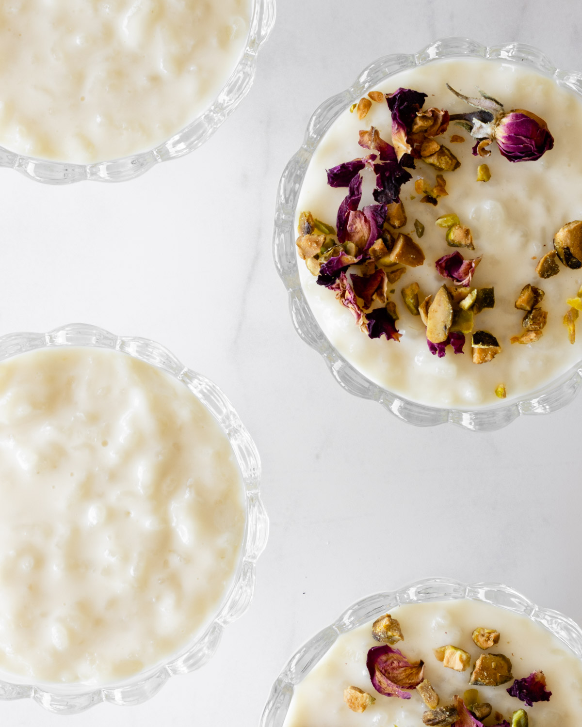 four small glass dishes with lebanese rice pudding and its garnishes.