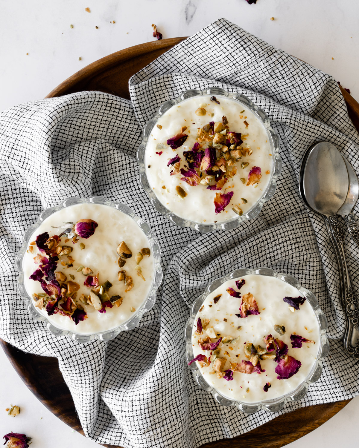 three bowls of lebanese rice pudding on a round wooden plate with a linen napkin and spoons.