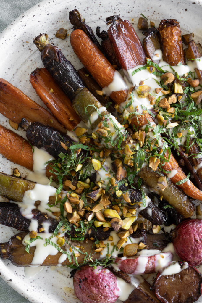 roasted rainbow carrots and radishes garnished with tahini sauce, fresh mint, and pistachios in a serving platter.