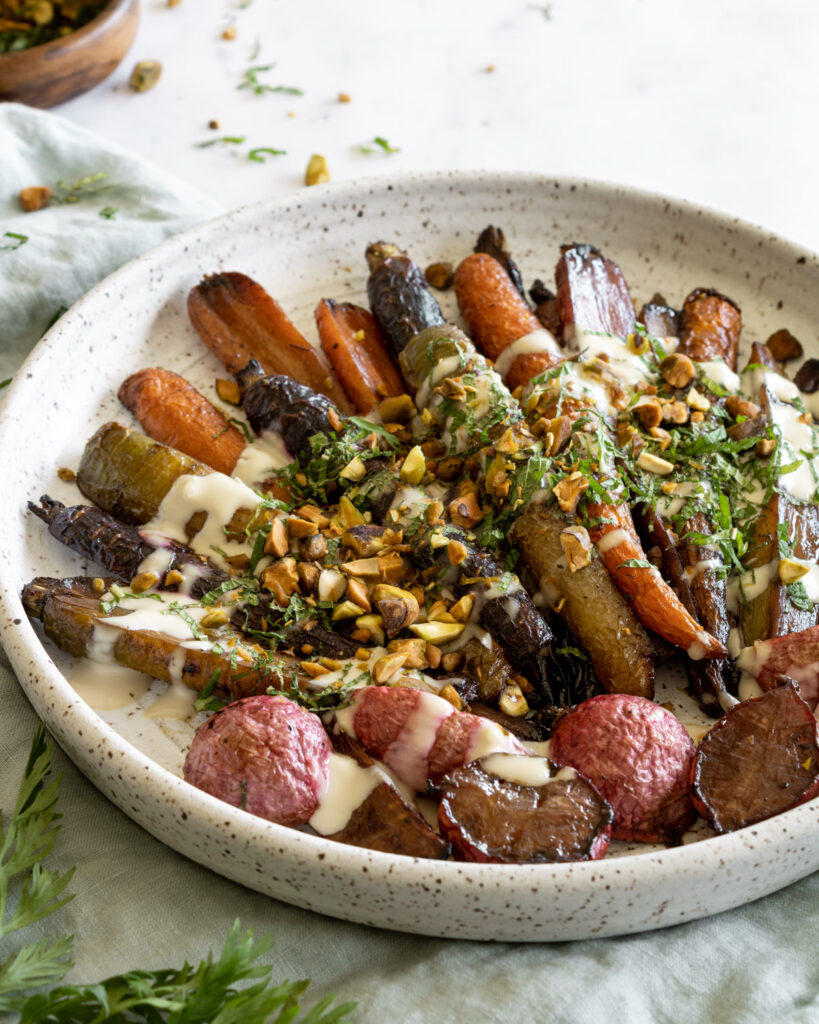 roasted rainbow carrots and radishes garnished with tahini sauce, fresh mint, and pistachios in a serving platter.