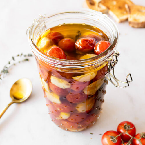 tomato confit in a tall jar with cherry tomatoes on the side and bread in the background