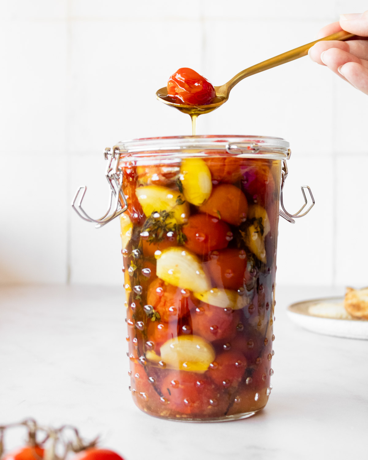 hand scooping out tomato confit with a gold spoon and oil dripping.