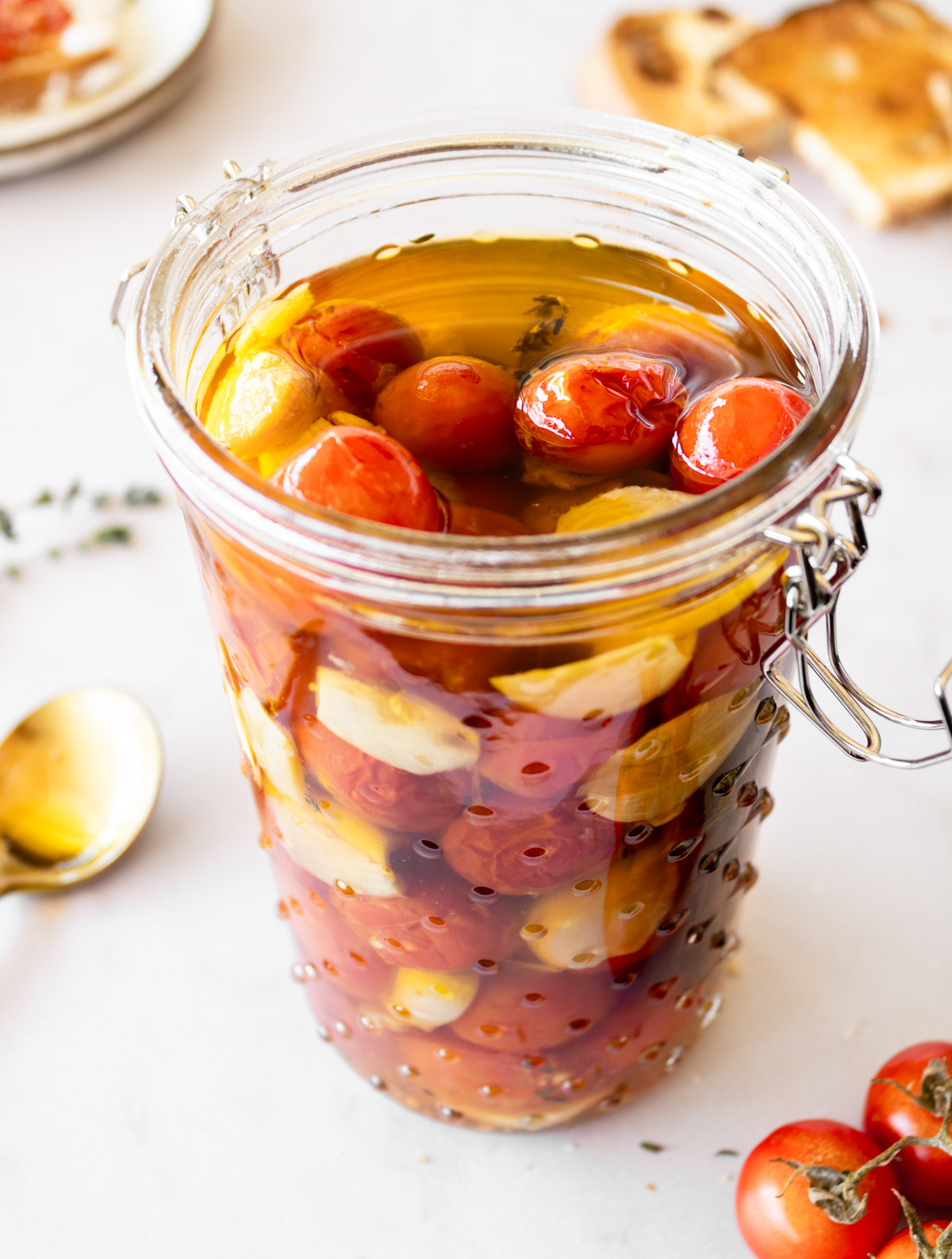 tomato confit in a tall jar with cherry tomatoes on the side and bread in the background