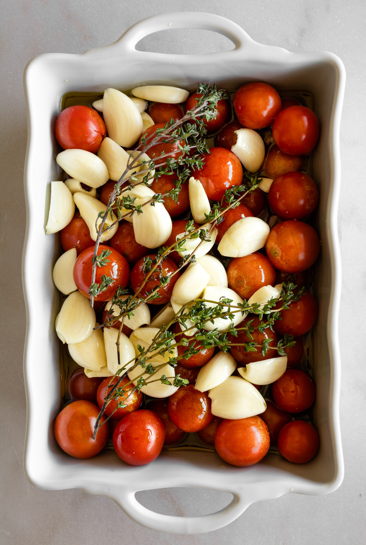 cherry tomatoes, garlic, and fresh thyme in a white baking dish.