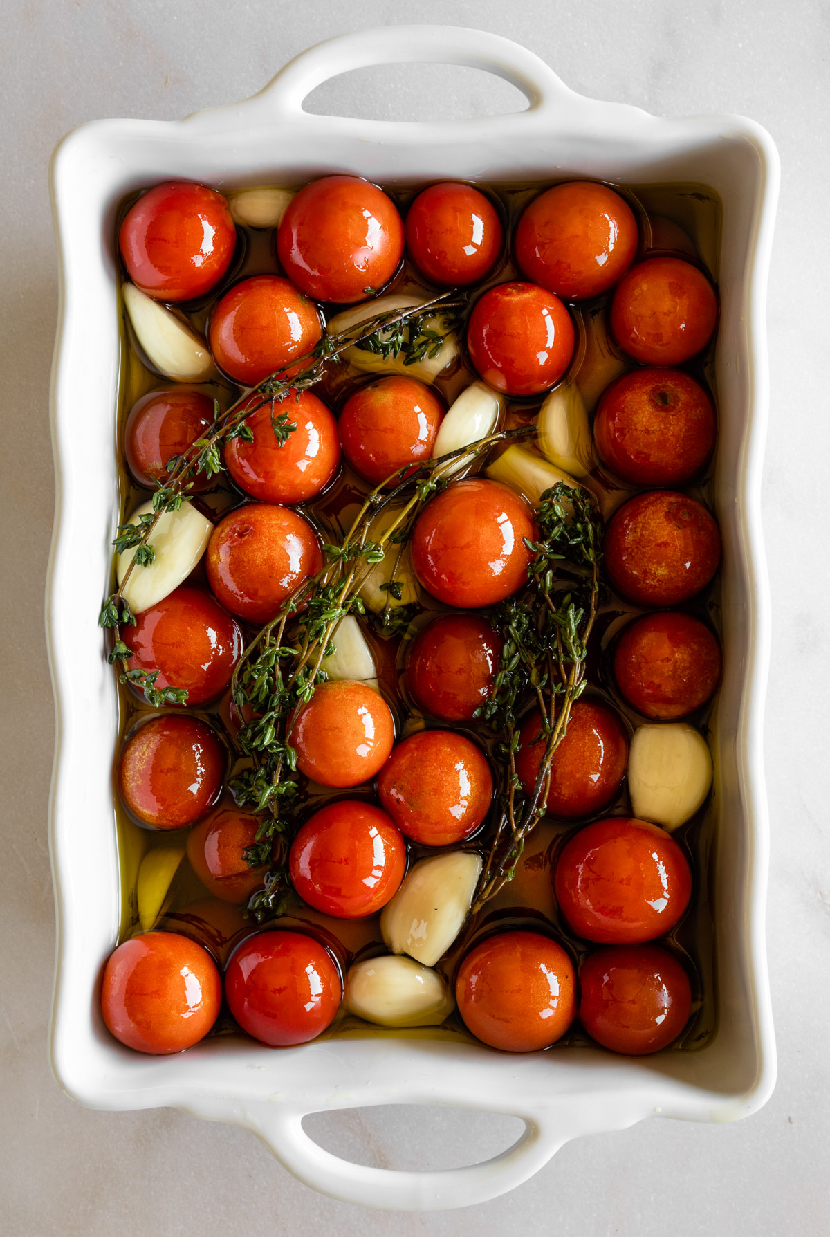 cherry tomatoes, garlic, fresh thyme, and olive oil in a white baking dish.