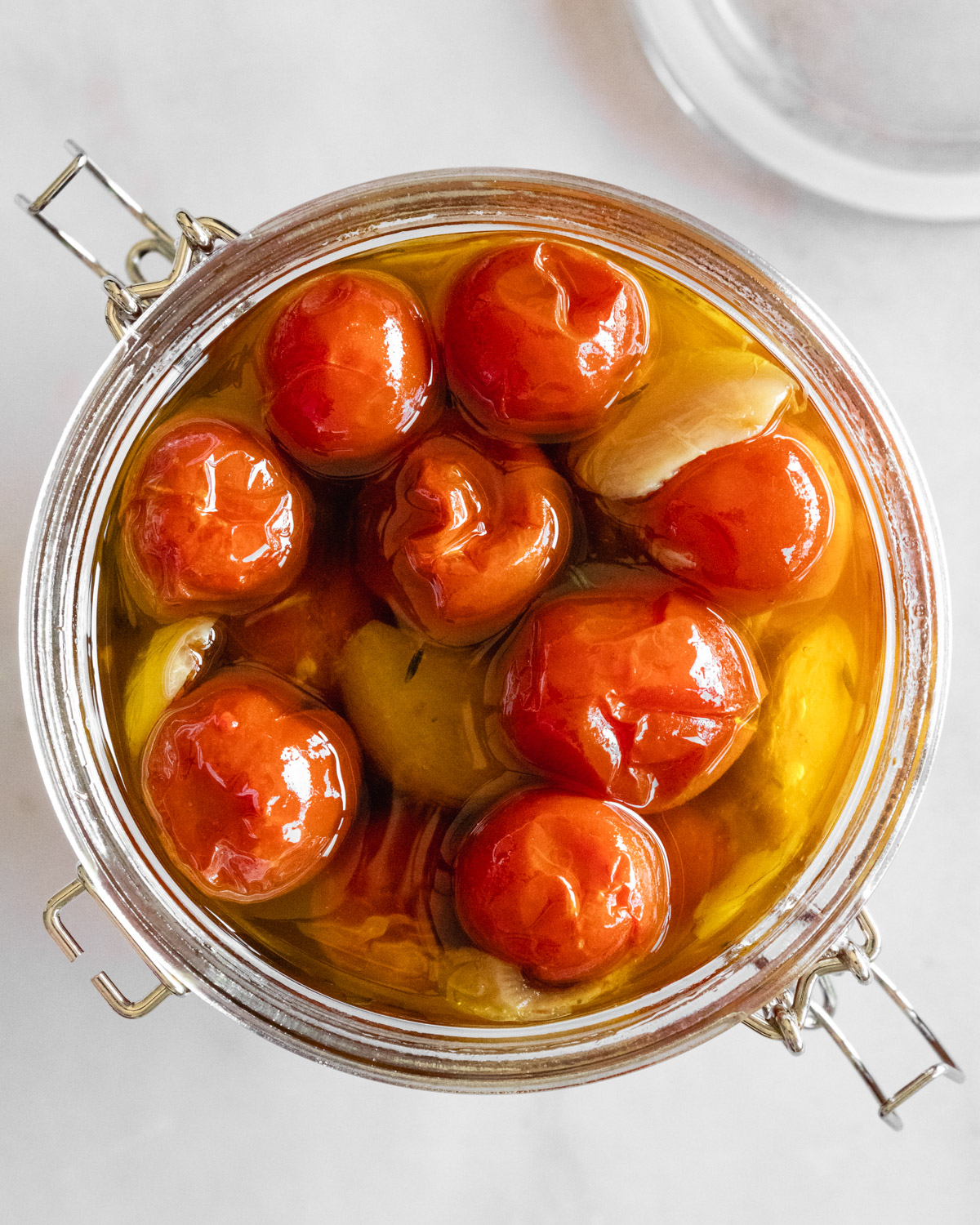 overhead view of tomato confit with garlic in a jar topped with olive oil.