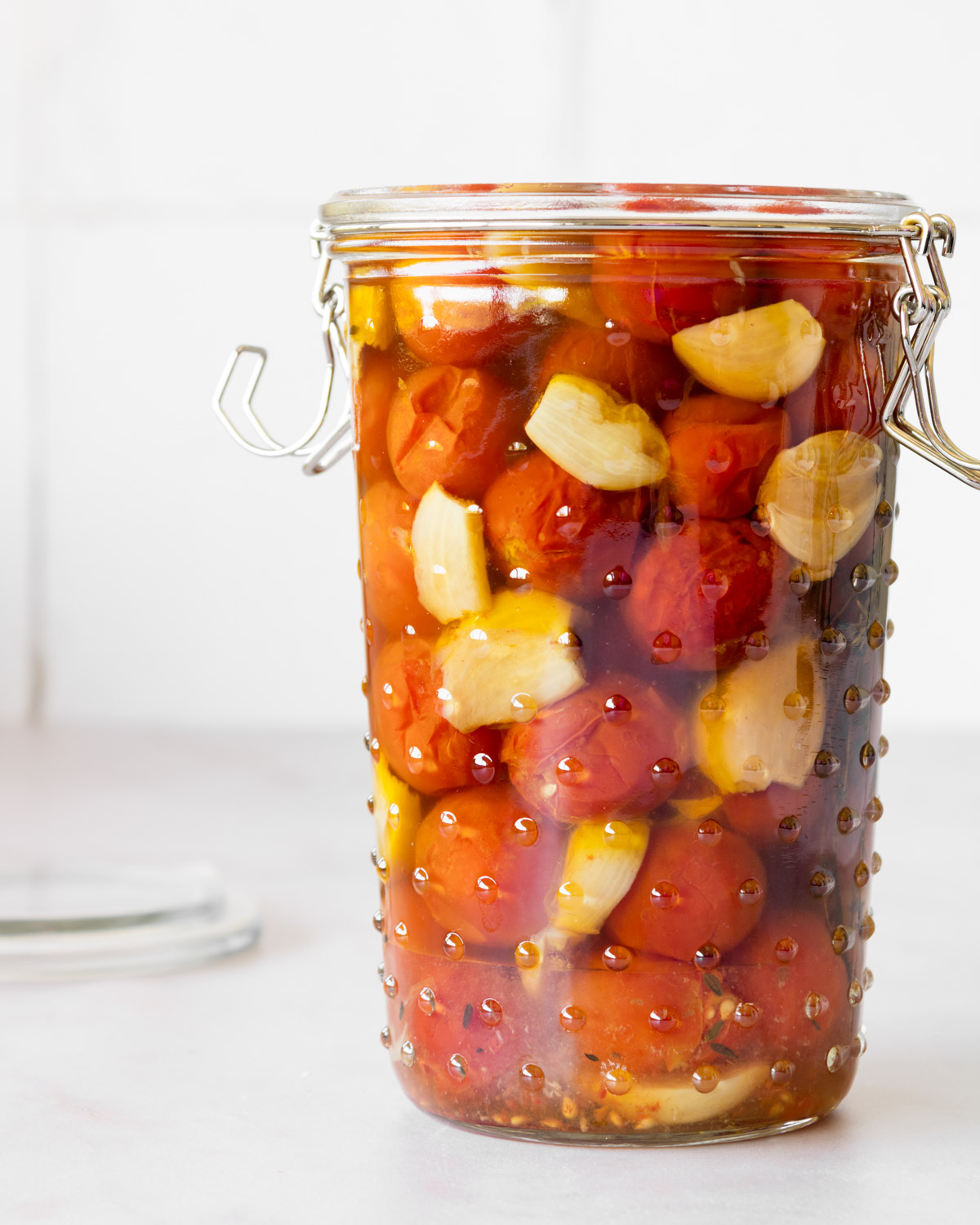 a tall jar of cherry tomato confit with garlic on a white counter,