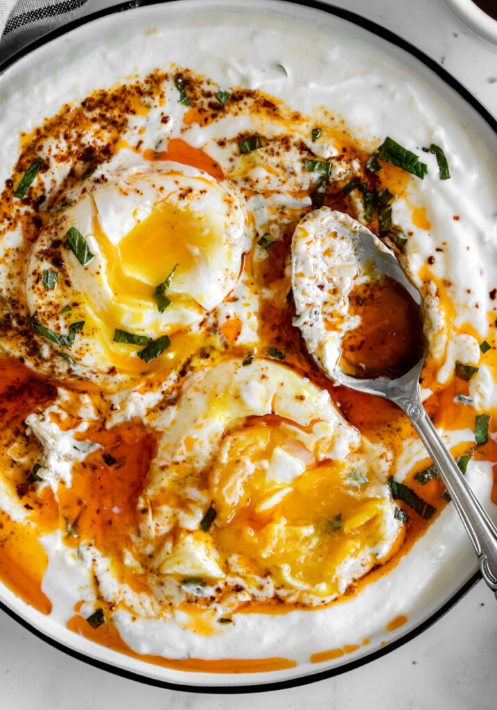 close up of turkish eggs with runny yolks and a dirty spoon.