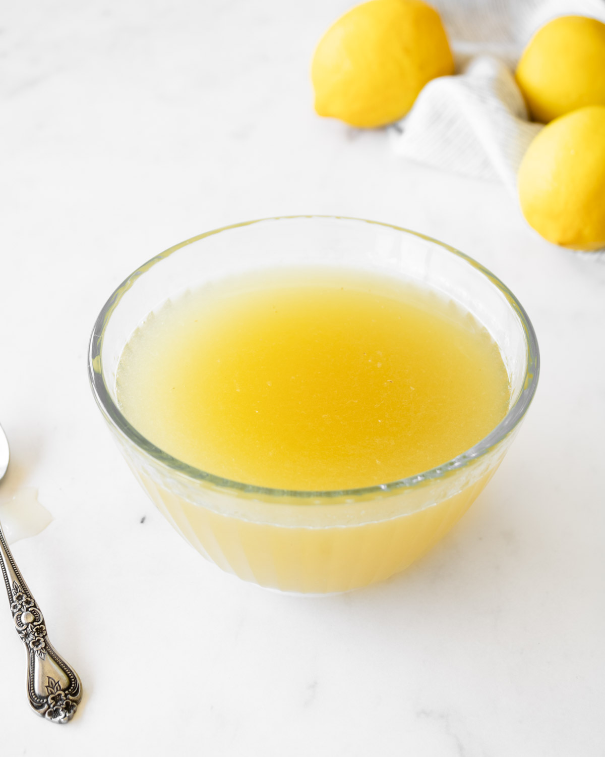 lemon sugar syrup in a glass bowl with lemons in the back.