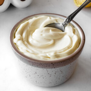 homemade mayonnaise in a small ceramic bowl with a spoon scooping some out.