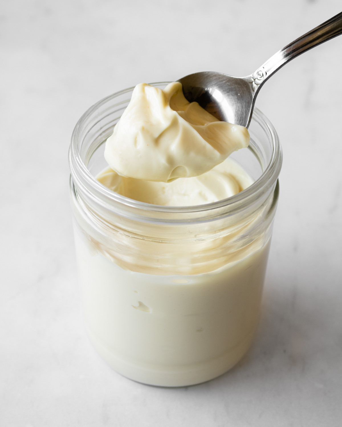 homemade mayonnaise in a glass jar with a spoon scooping some out.