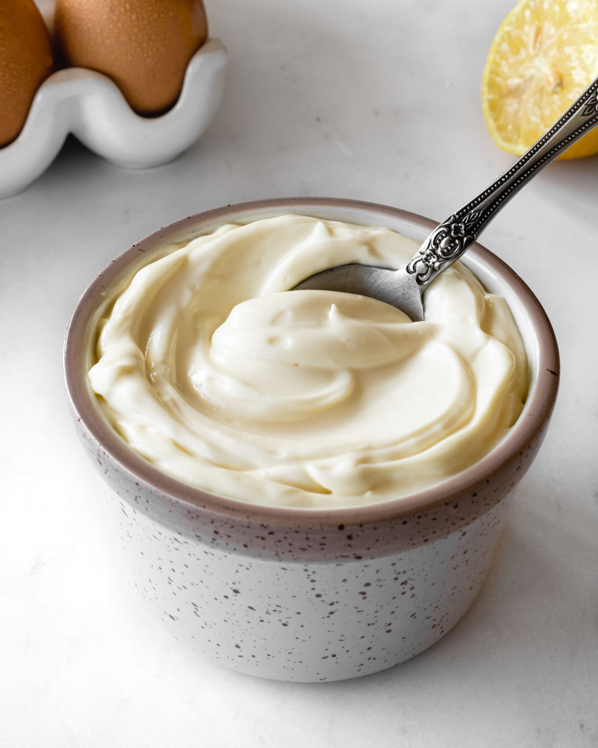 homemade mayonnaise in a small ceramic bowl with a spoon scooping some out.