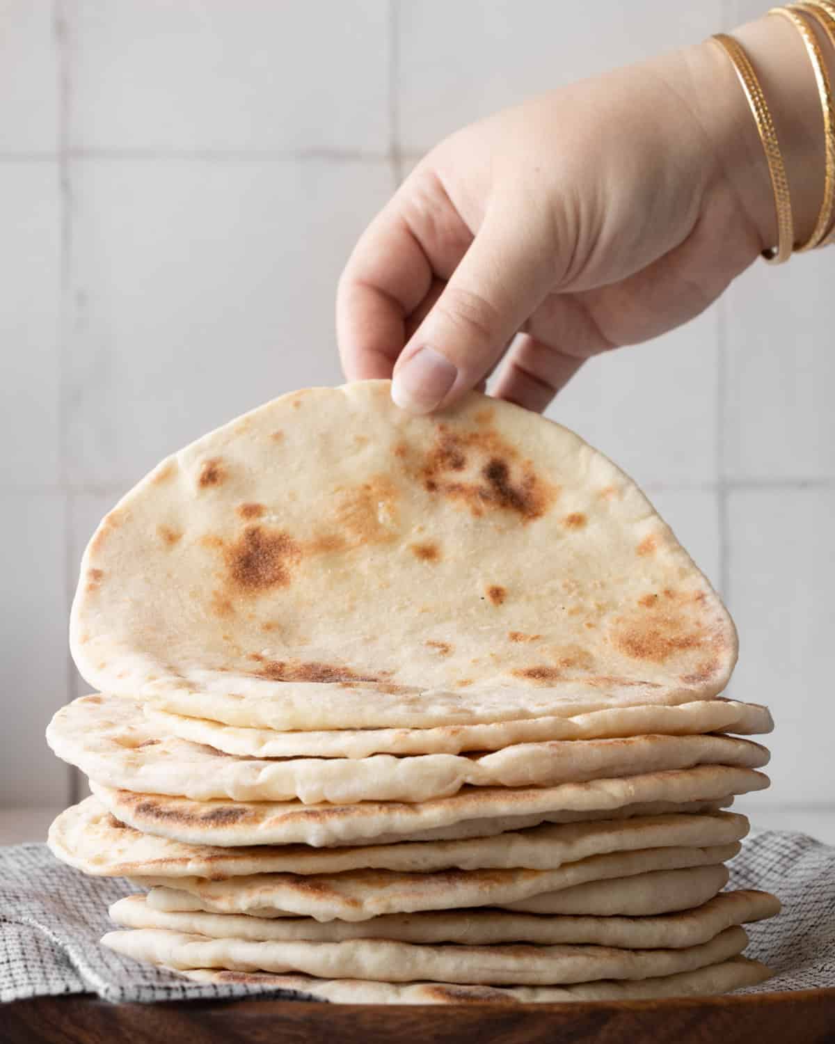hand picking up a pita bread from a stack of pita on a plate.