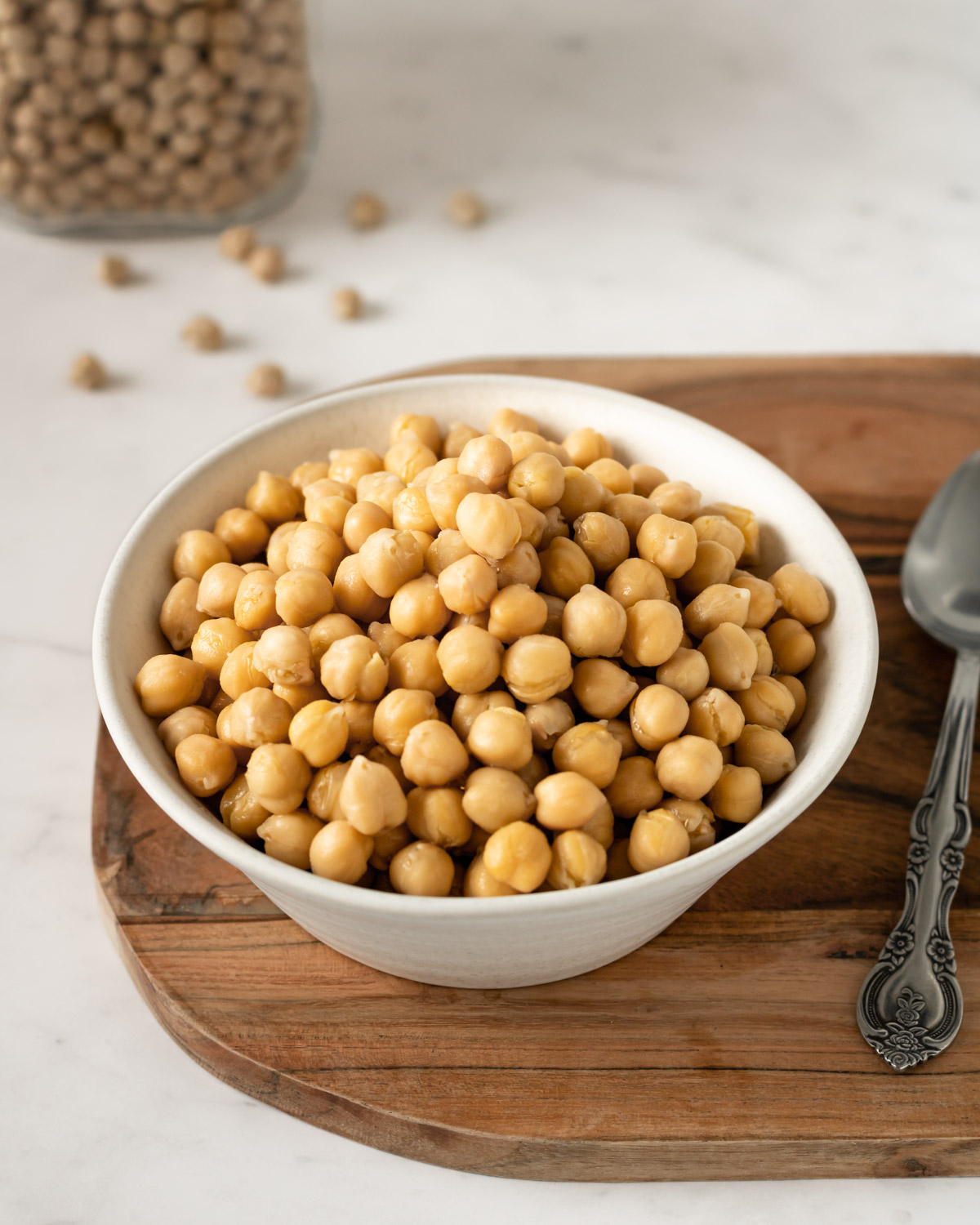 bowl of cooked chickpeas on a wooden board with a spoon on the side.