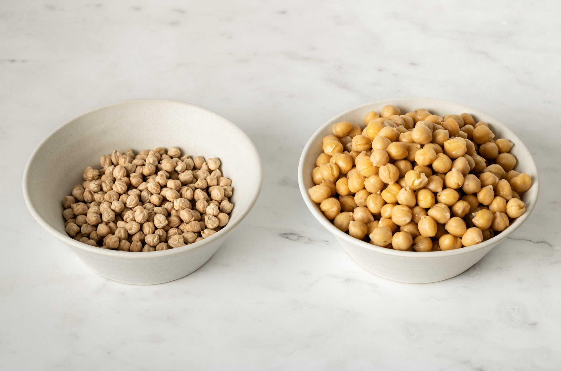 a bowl of dried chickpeas next to a bowl of cooked chickpeas for volume comparison.