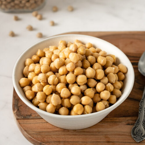 bowl of cooked chickpeas on a wooden board with a spoon on the side.