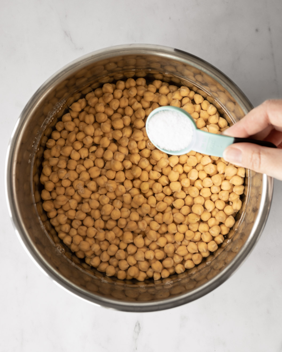 hand adding salt to pot of soaked chickpeas before cooking.