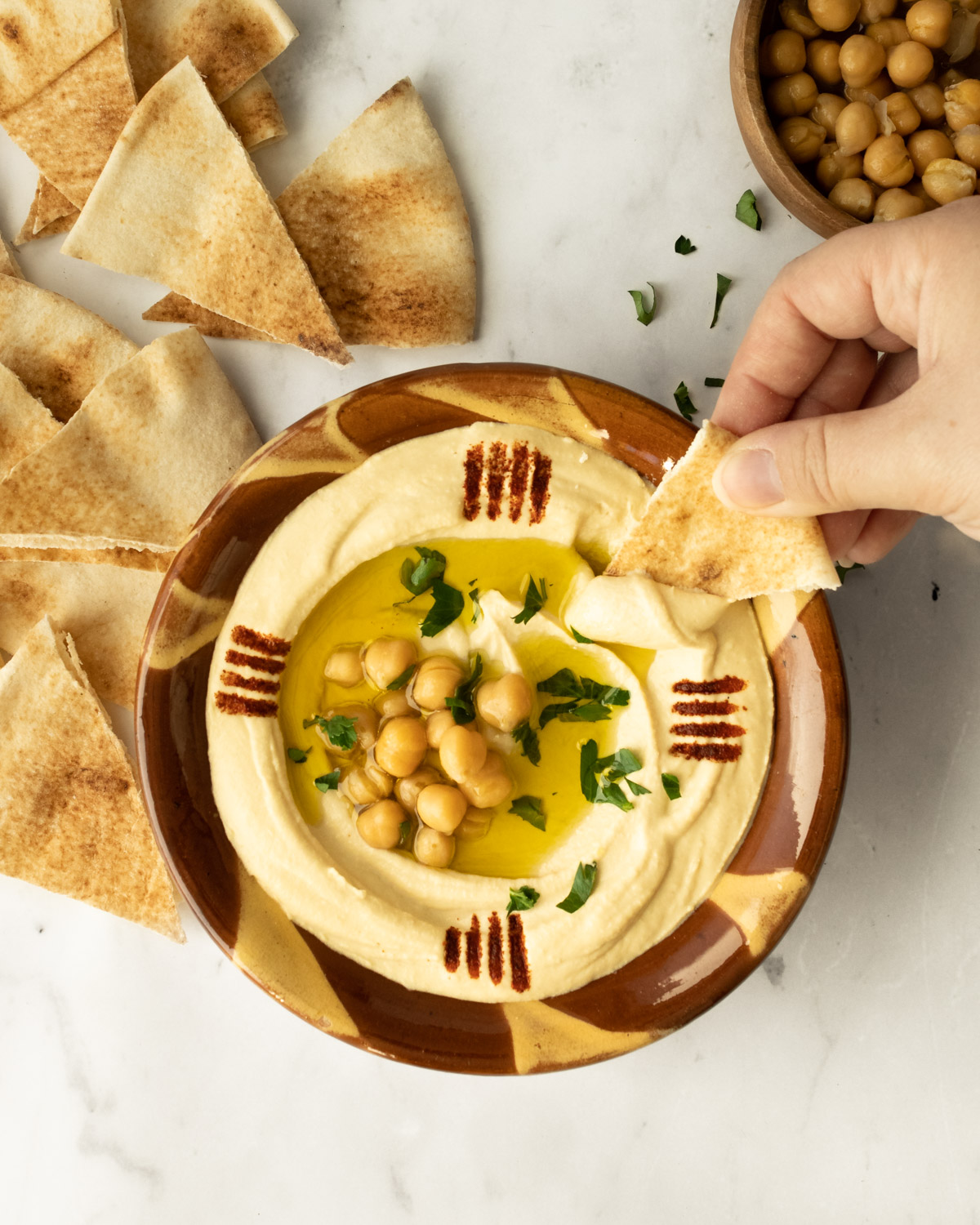 hand dipping pita bread into a bowl of creamy hummus.