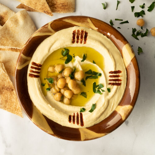 hummus in a traditional Lebanese clay bowl with garnishes.