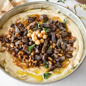 spiced meat and pine nuts on top of hummus in a shallow bowl.
