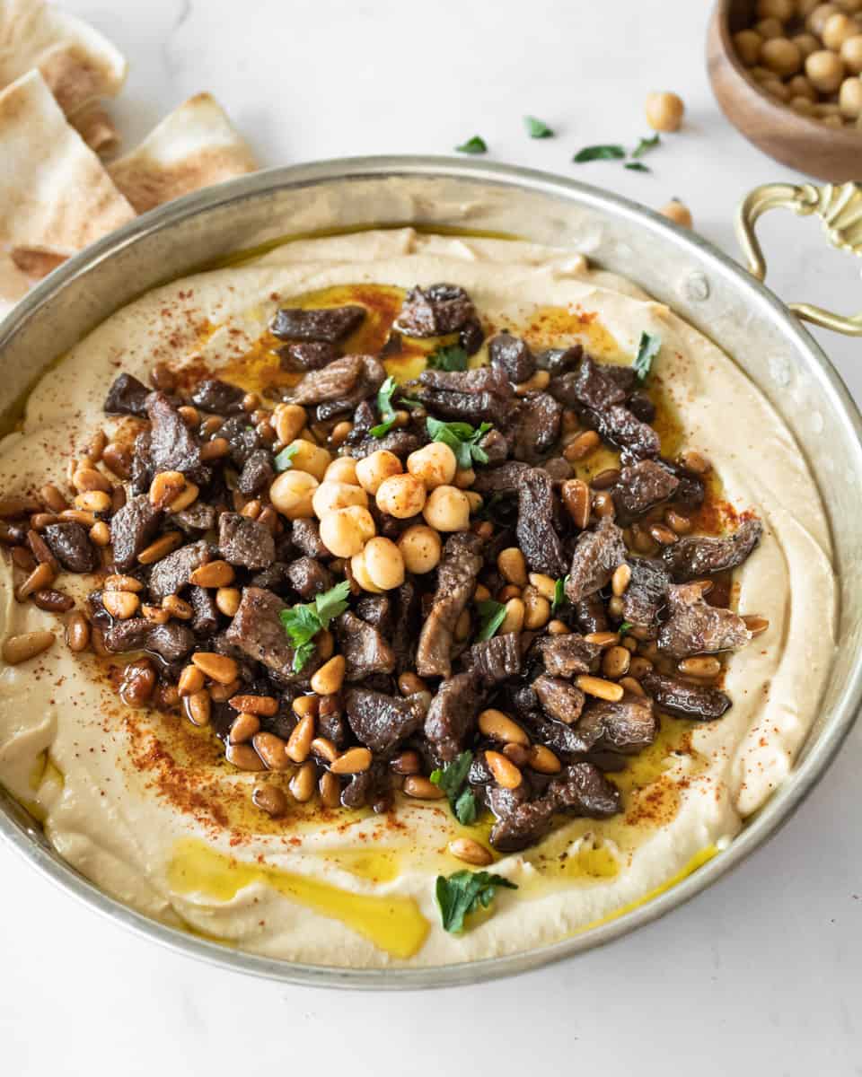 spiced meat and pine nuts on top of hummus in a shallow bowl.