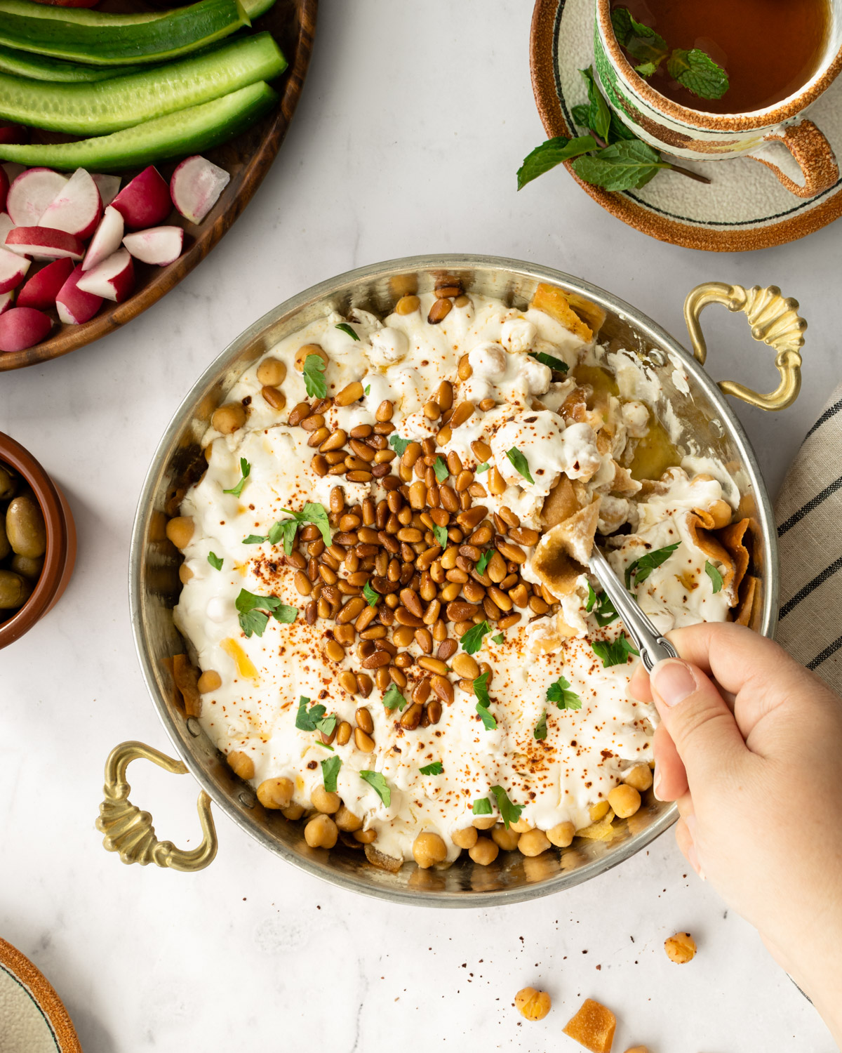 hand scooping up chickpea fatteh with a spoon.