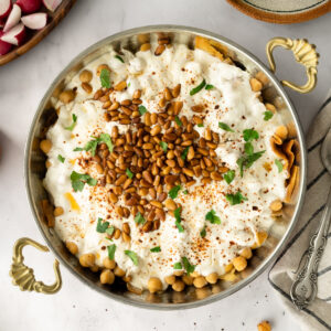 chickpea fatteh in a bowl surrounded by fresh veggies, tea, and a cloth napkin.