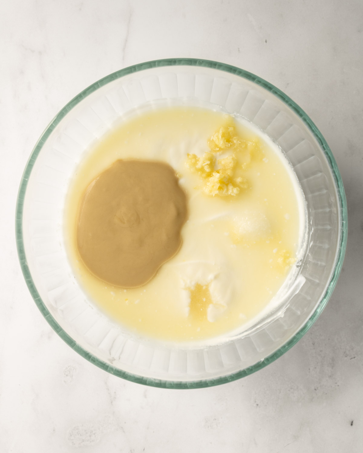 a glass bowl with yogurt, tahini, garlic, and lemon juice before mixing.