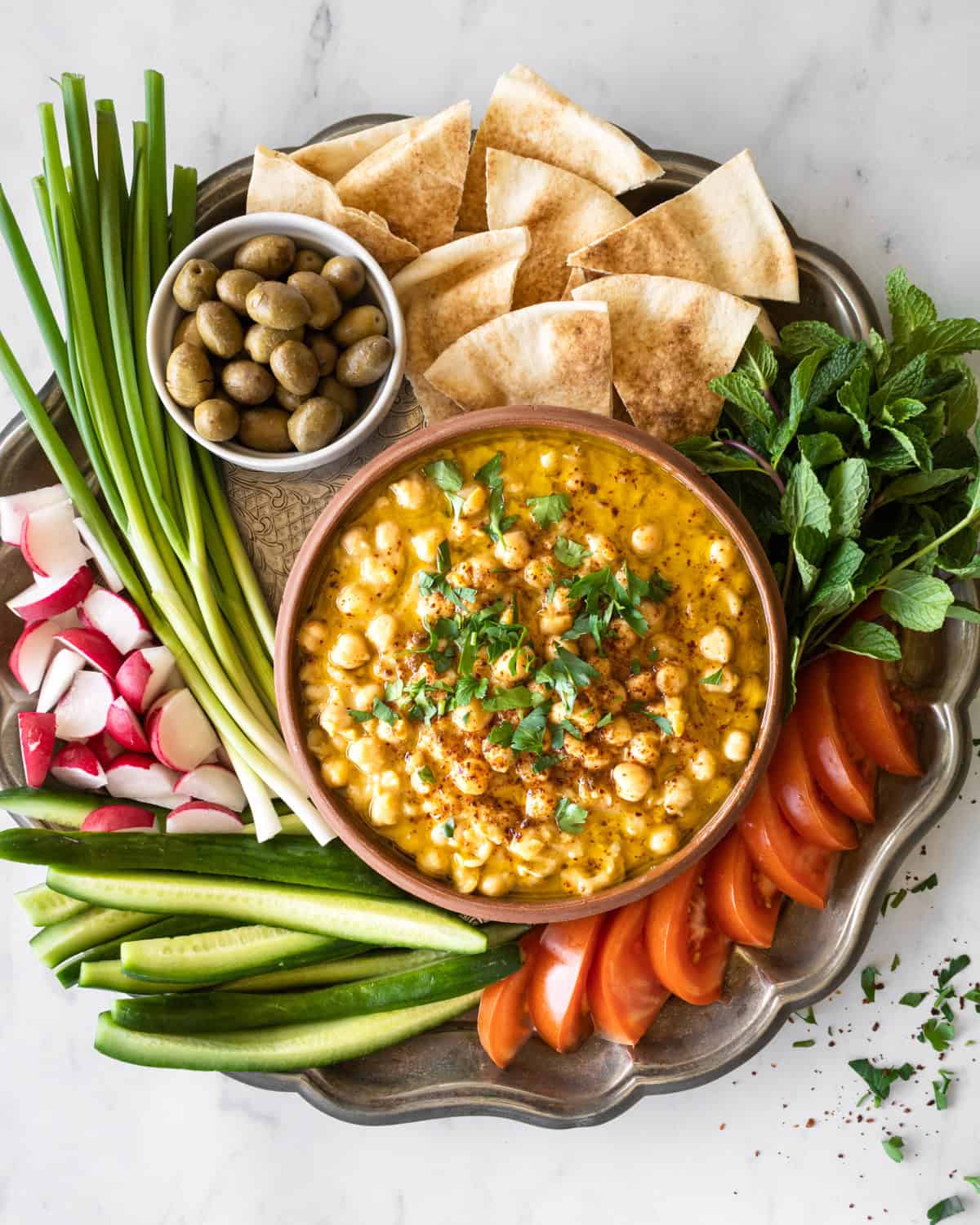 balila in a bowl on a tray with fresh veggies and pita bread.