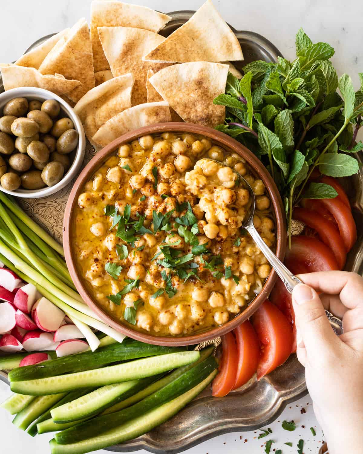 traditional hummus balila in a bowl with fresh veggies and pita bread on the side.