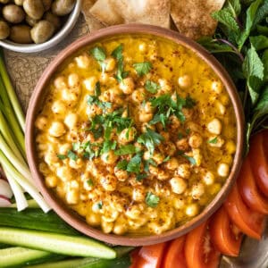 traditional hummus balila in a bowl with fresh veggies and pita bread on the side.