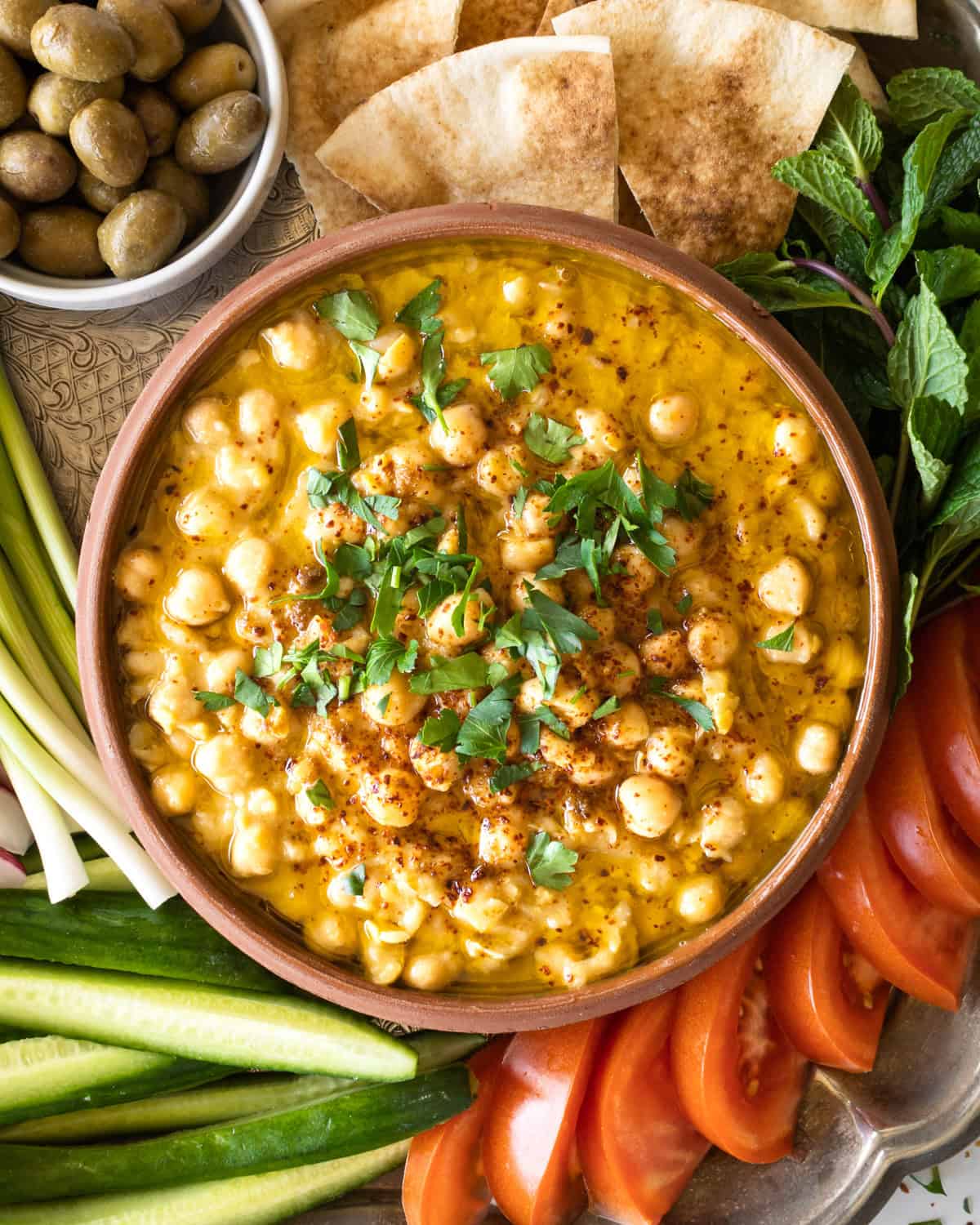 traditional hummus balila in a bowl with fresh veggies and pita bread on the side.