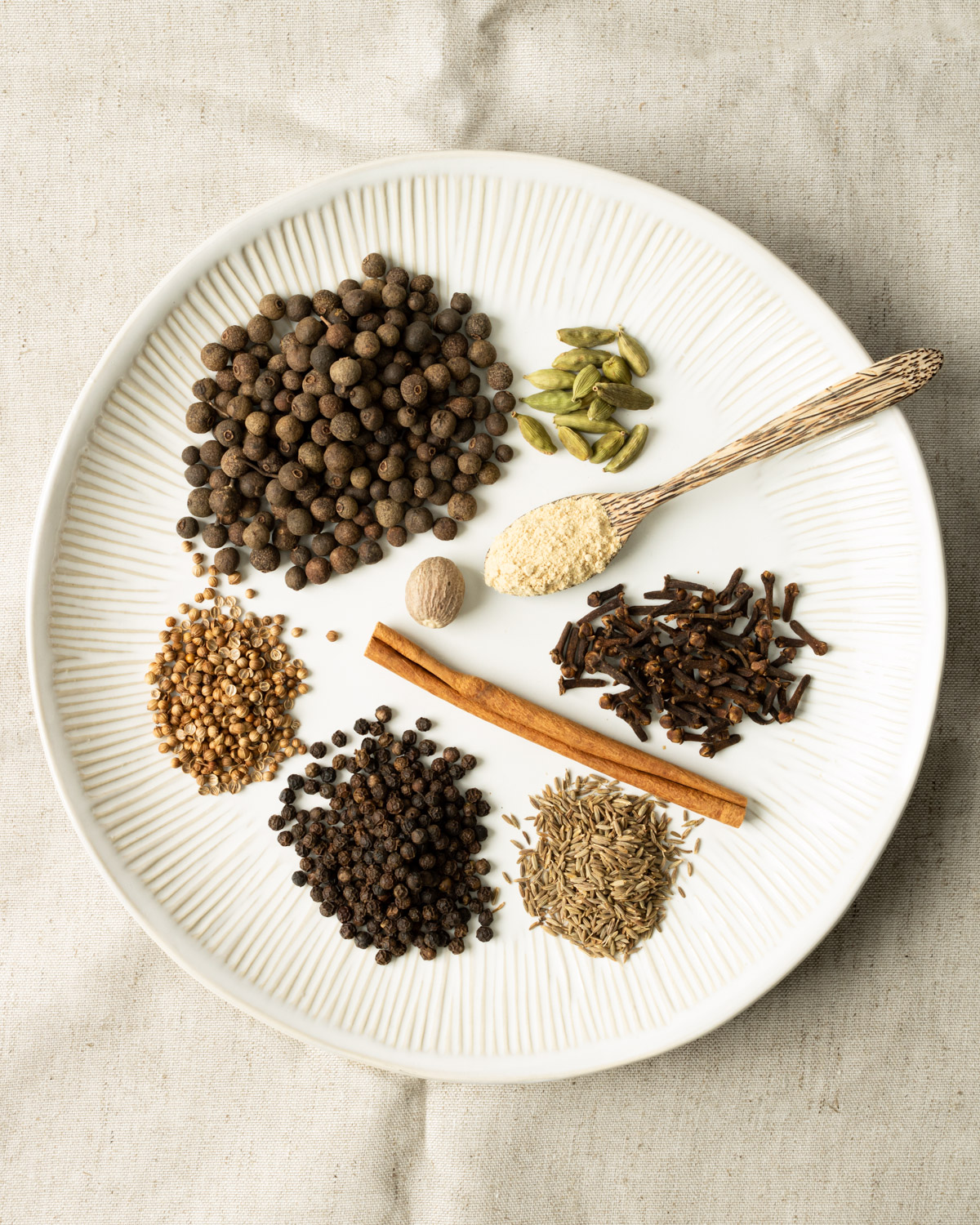 a variety of whole spices on a white plate for Lebanese 7 spice.